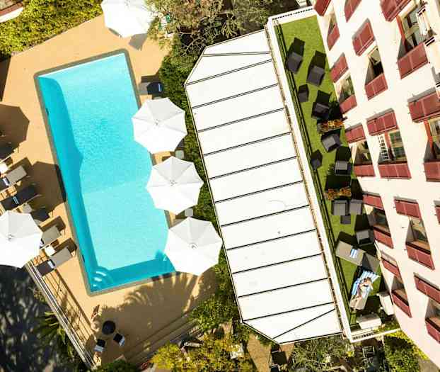 Bild av en pool, solstolar och parasoller vid sidan av en byggnad. (AI-genererad text)