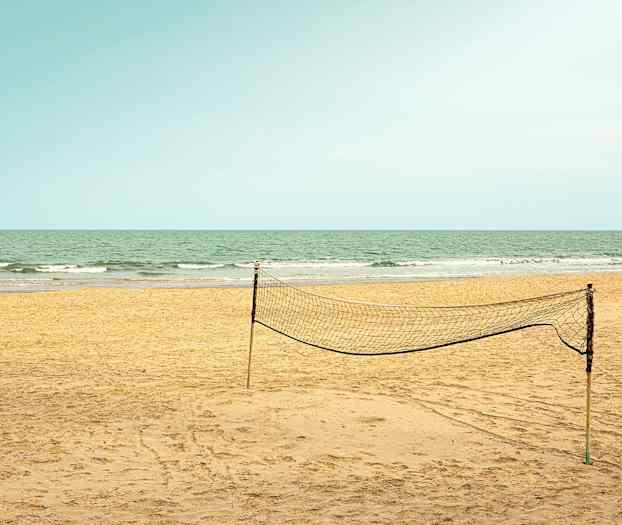En tom sandstrand med ett uppsatt volleybollnät och havet i bakgrunden. (AI-genererad text)