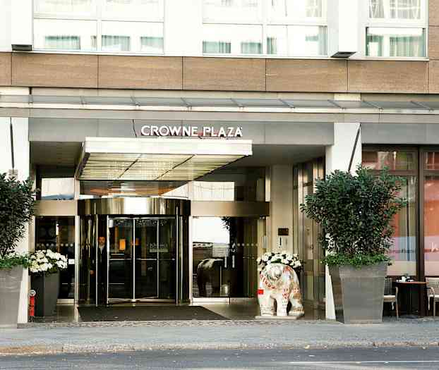 Ingången till hotell Crowne Plaza med glasdörrar och stora blomkrukor. (AI-genererad text)