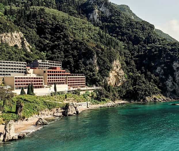 Hotell beläget vid en klippig kust omgiven av grönskande berg. (AI-genererad text)