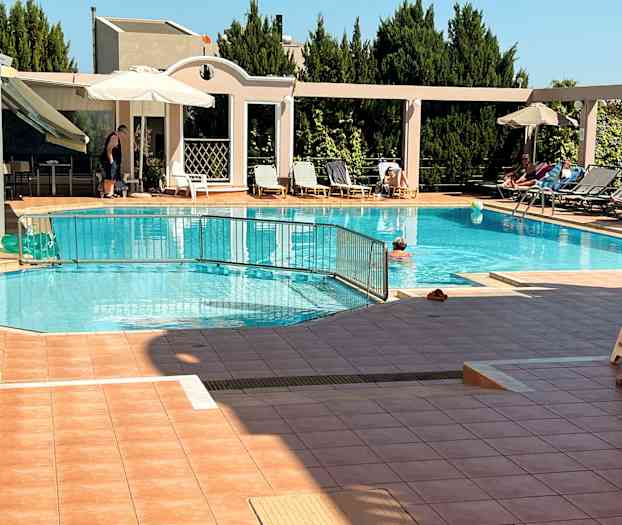 Utomhuspool med solstolar och parasoll vid sidan av, samt människor som badar och solar. (AI-genererad text)