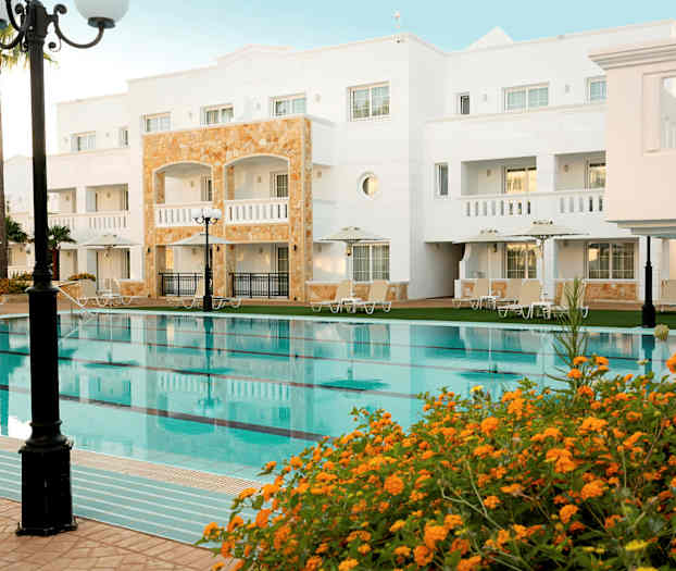 Hotellbyggnad med pool och omgivande solsängar. (AI-genererad text)