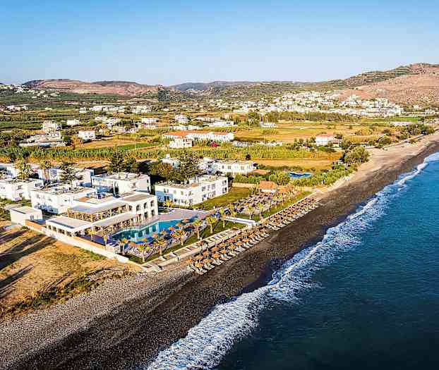 Vy över en strand med parasoller, solstolar och en resort med pooler i närheten. (AI-genererad text)