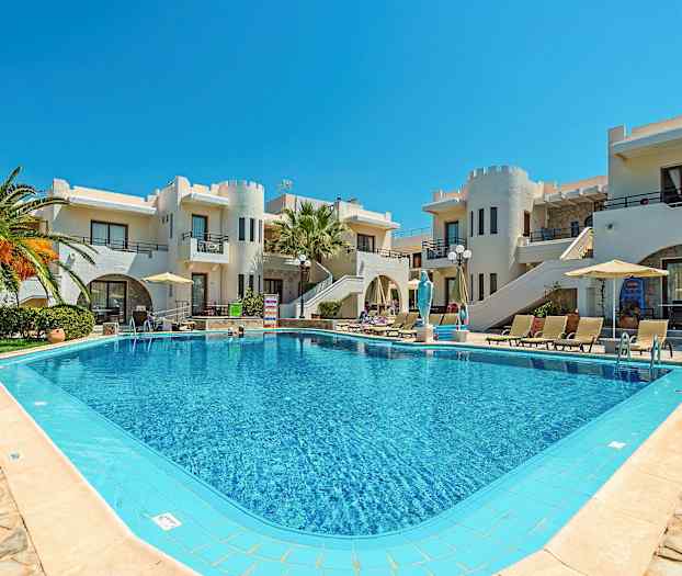 En pool omgiven av solstolar och parasoller framför byggnader med vit fasad och unika arkitektoniska detaljer. (AI-genererad text)