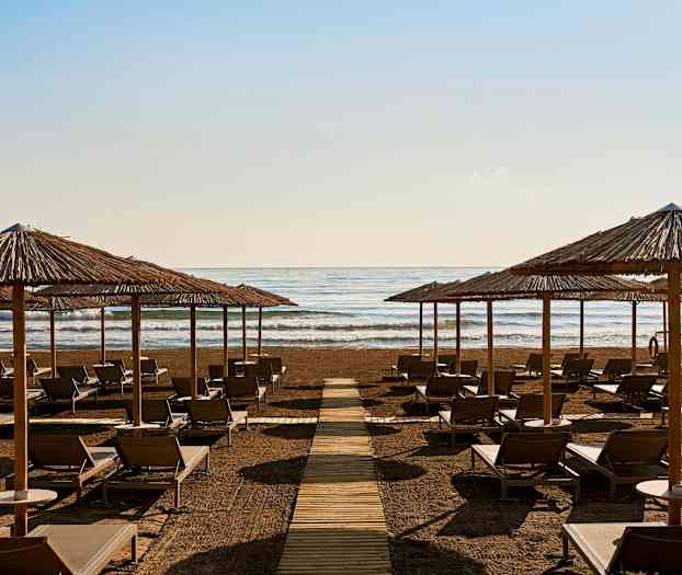 Solstolar och parasoller på en strand framför havet. (AI-genererad text)