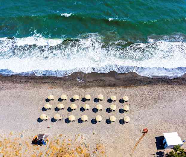 Flygfoto av en strand med paraplyer och vågor. (AI-genererad text)