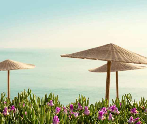 Två strandparasoller med havsbakgrund och blommor i förgrunden. (AI-genererad text)