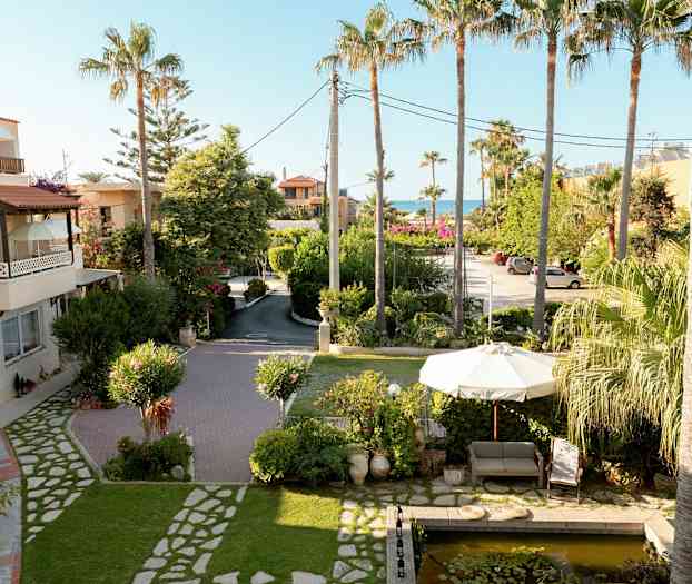 Bild av en trädgård med en soffa och parasoll nära en liten damm, omgivna av palmer och grönska. (AI-genererad text)