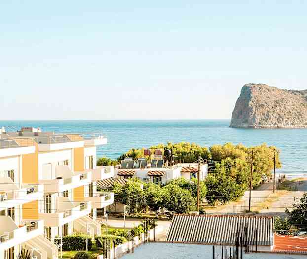 Utsikt över byggnader, grönska och hav med en klippa i bakgrunden. (AI-genererad text)