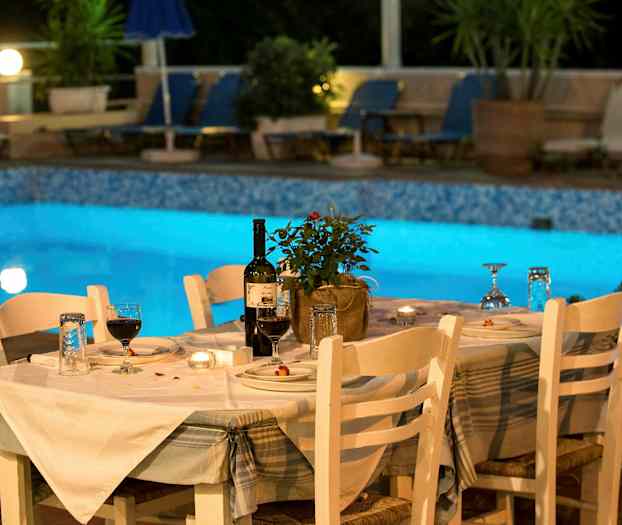 Ett dukat bord med vita stolar vid sidan av en upplyst pool. (AI-genererad text)