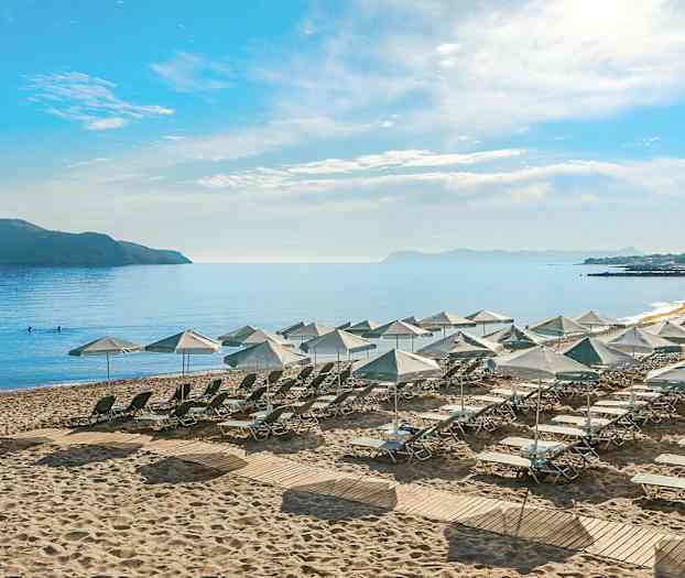 Utsikt över en strand med solstolar och parasoller, omgivande hav och en avlägsen ö. (AI-genererad text)