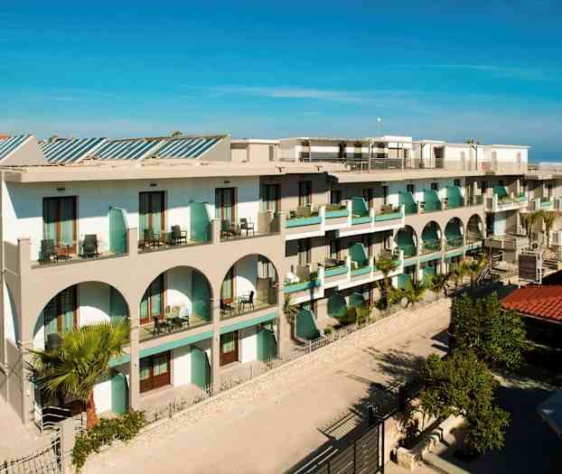 Bild av ett hotell med balkonger och arkitektoriska valv, omgiven av grönska. (AI-genererad text)