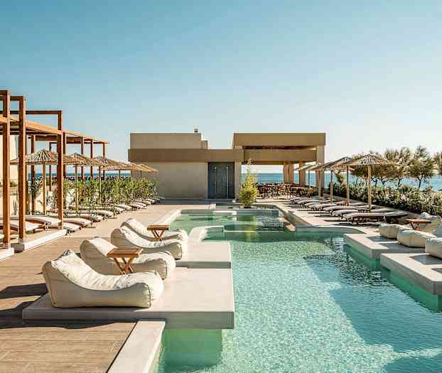 Utomhuspool med solstolar och parasoller vid sidan, med havet i bakgrunden. (AI-genererad text)