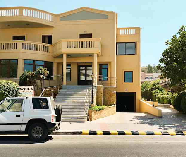 En bil står parkerad framför en byggnad med en skylt med texten 'Achilles Plaza'. (AI-genererad text)