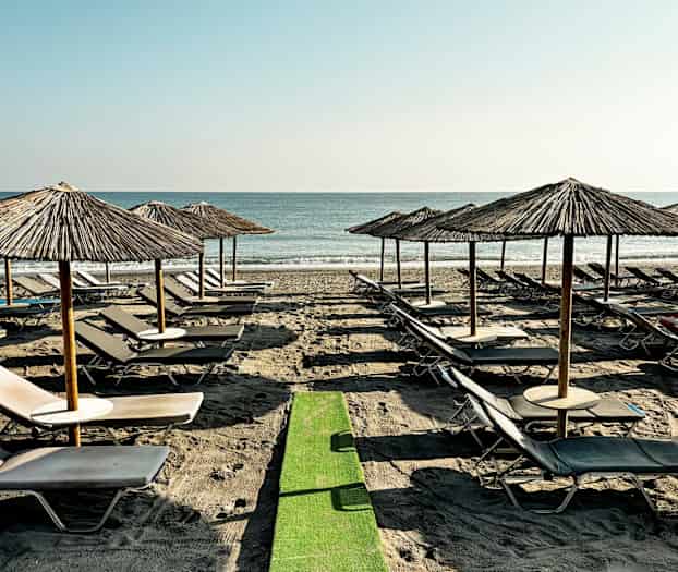 Strand med solstolar och parasoller i rad vid havet. (AI-genererad text)