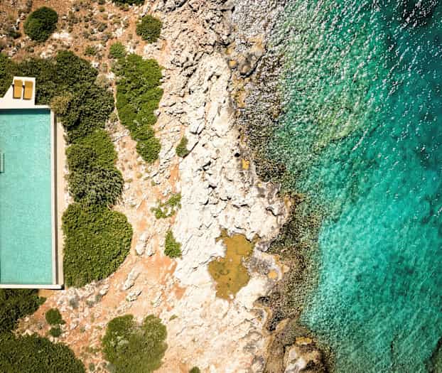 En pool bredvid klippor och hav från ovan. (AI-genererad text)