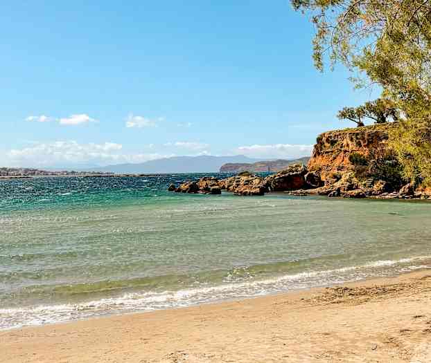Sandstrand med turkost hav, stenklippor och gröna träd. (AI-genererad text)