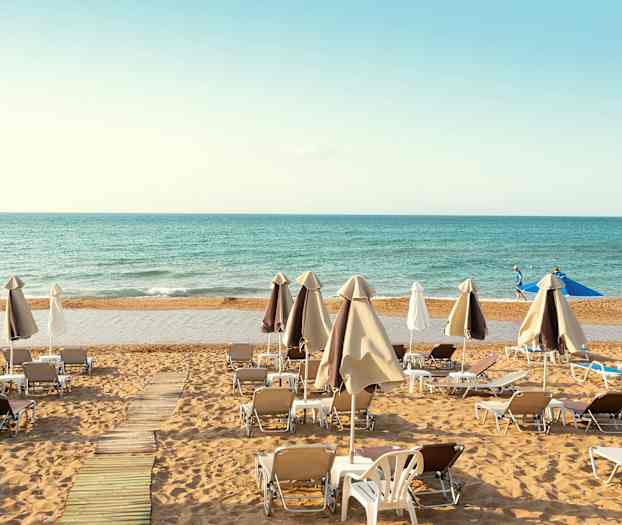 Solstolar och parasoller uppställda på en sandstrand med havet i bakgrunden. (AI-genererad text)
