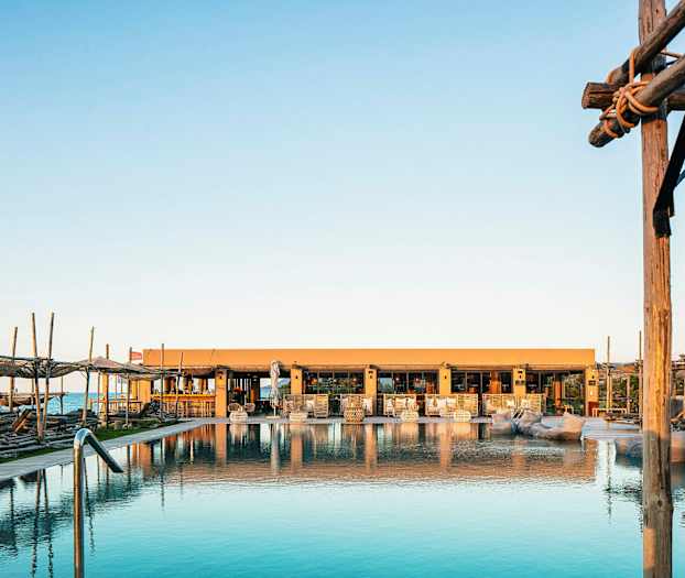 Bild av en pool med solstolar och ett hus i bakgrunden vid soluppgång eller solnedgång. (AI-genererad text)