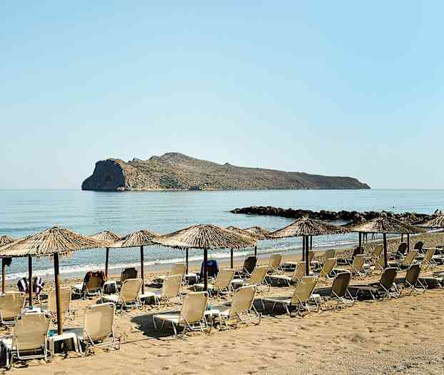 Solstolar och parasoller på en sandstrand med en klippa i havet. (AI-genererad text)