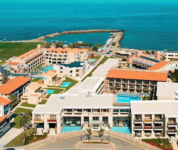 Flygbild över ett hotellkomplex vid kusten med pooler, byggnader och havet i bakgrunden. (AI-genererad text)