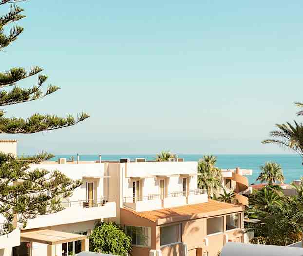 Vy över träd, byggnader och hav under en klar himmel. (AI-genererad text)