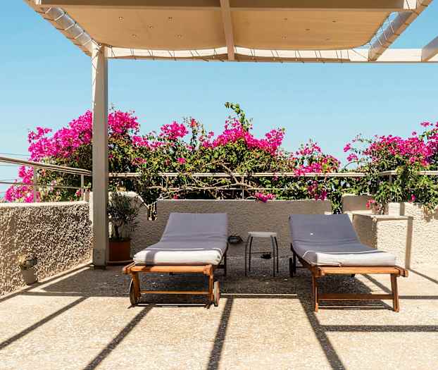 Terrass med två solstolar, bougainvillea och takavsats under blå himmel. (AI-genererad text)