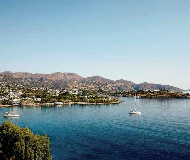 Landskap med en lugn vik, segelbåtar och små byggnader vid foten av berg. (AI-genererad text)