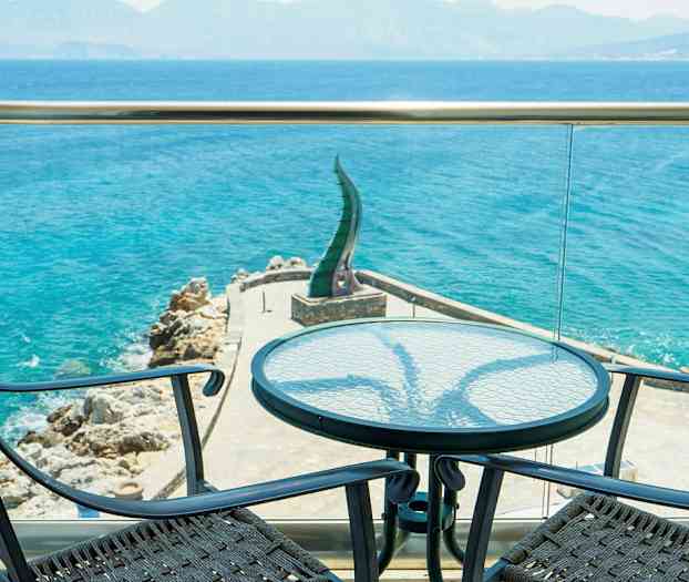 Utsikt från en terrass mot havet med två stolar och ett bord i förgrunden. (AI-genererad text)