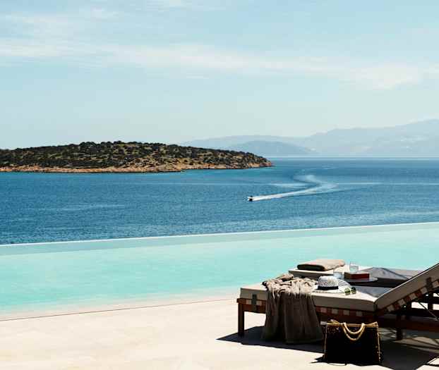 Solstolar vid en infinitypool med utsikt över havet och en liten ö. (AI-genererad text)