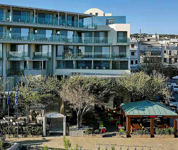 Ett modernt hotell med balkonger och en uteservering med sittplatser under tak och öppet himmel, omringat av träd. (AI-genererad text)