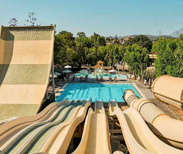 Bild av en vattenpark med flera vattenrutschbanor som leder ner till en pool omgiven av gröna träd. (AI-genererad text)