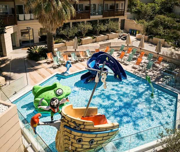 En pool med barnvänliga figurer och en rutschkana, omgiven av solstolar och en palm. (AI-genererad text)
