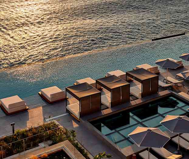 Vy över solstolar och skuggande parasoller vid en infinitypool med havet i bakgrunden. (AI-genererad text)