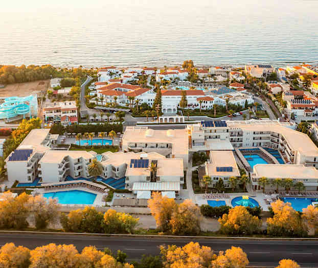 Flygvy över ett semesterhotell med flera pooler och vattenrutschkanor vid havet. (AI-genererad text)