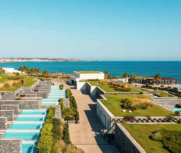 Utsikt över en semesteranläggning vid havet med privata pooler och grönska. (AI-genererad text)