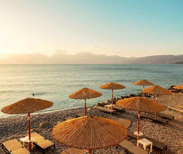 Strand med solstolar och parasoller samt utsikt över havet vid solnedgång. (AI-genererad text)