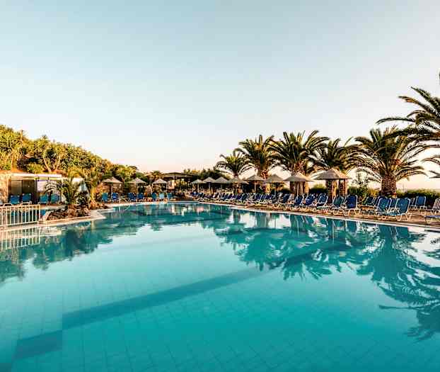 En utomhuspool omgiven av solstolar och paraplyer, med palmer och växter i bakgrunden. (AI-genererad text)