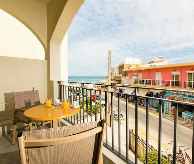 En balkong med bord och stolar, med utsikt över gatan och havet. (AI-genererad text)