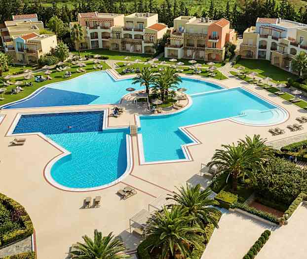 Vy över en stor utomhuspool omgiven av solstolar och parasoller, med byggnader i bakgrunden. (AI-genererad text)