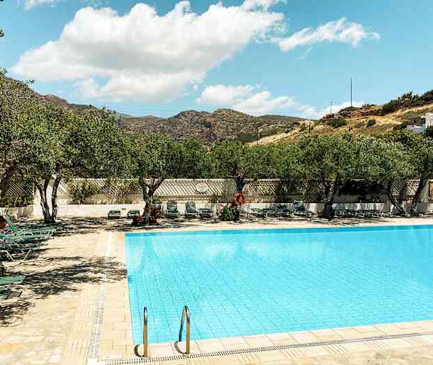 En utomhuspool omgiven av solstolar och träd under en klar himmel. (AI-genererad text)