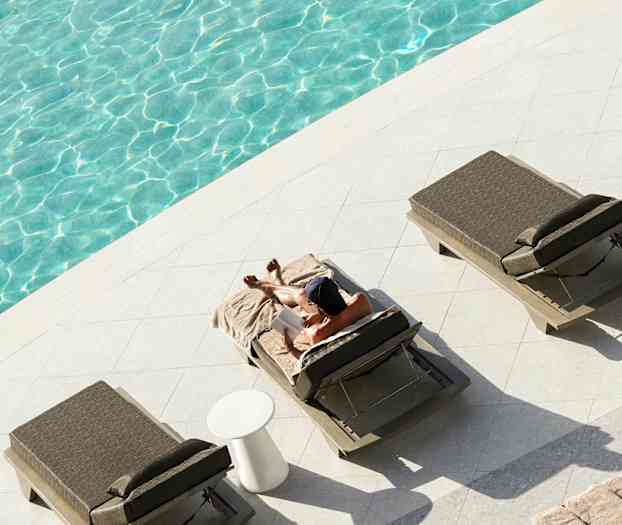 En person ligger och kopplar av på en solstol bredvid en pool. (AI-genererad text)
