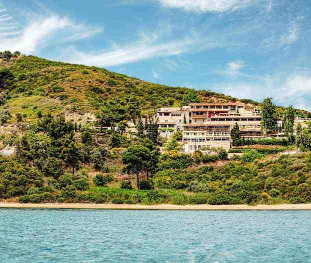 Hotellanläggning vid en grönskande sluttning nära vatten. (AI-genererad text)