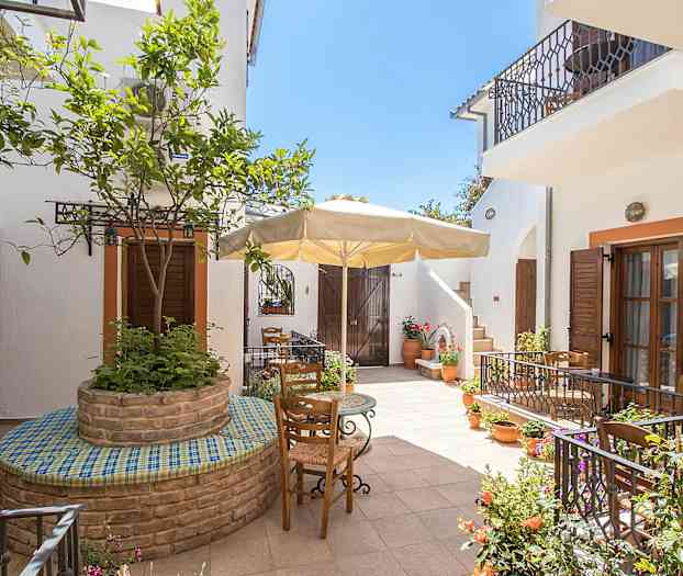 Innergård med blomkrukor, träd och utemöbler under ett parasoll. (AI-genererad text)