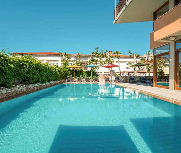 Utomhuspool med omgivande grönska och möblerade områden. (AI-genererad text)