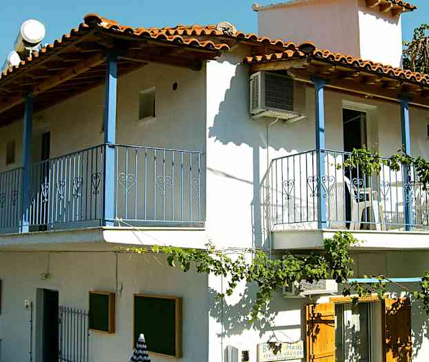 En tvåvåningsbyggnad med vit fasad, blå balkonger och röda takpannor. (AI-genererad text)