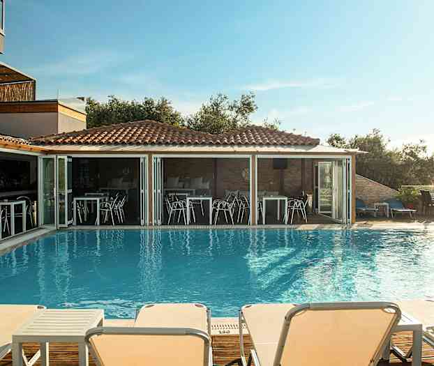 Utomhuspool med solstolar och en restaurang i bakgrunden. (AI-genererad text)