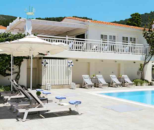 Vit byggnad med röda tak och poolområde med solstolar och parasoller. (AI-genererad text)