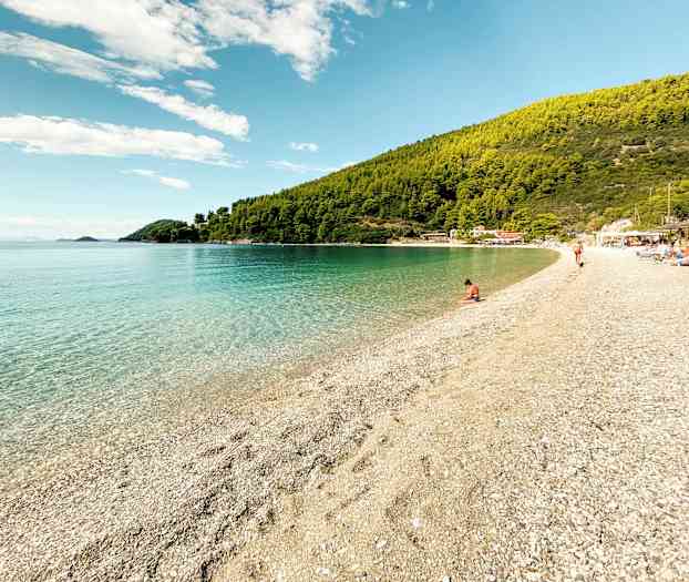 En lugn strand med klart vatten, omgiven av grönskande kullar. (AI-genererad text)