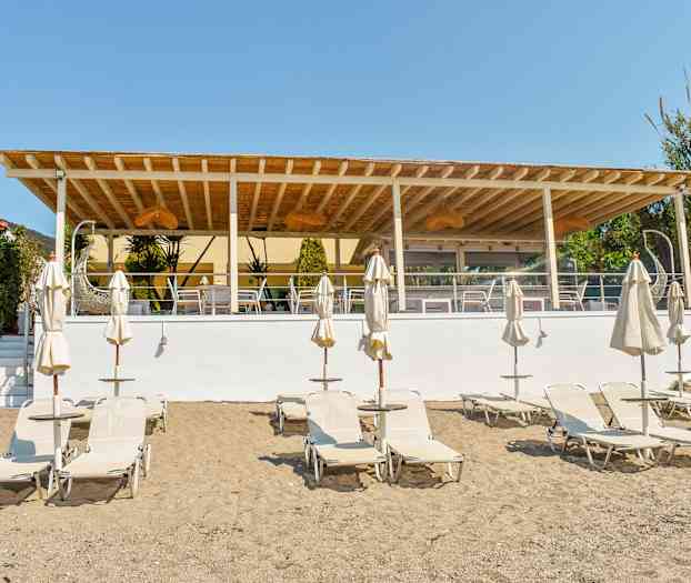 Strand med solstolar och parasoller framför en utomhusterrass. (AI-genererad text)